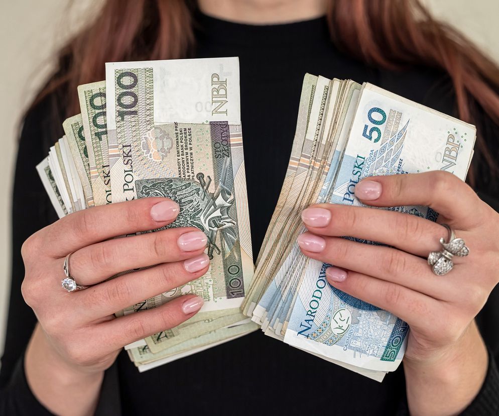 Dłonie kobiety trzymającej dwa pliki banknotów 100 i 50 złotych. O kradzieży w Kielcach przeczytasz na Eska Kielce.
