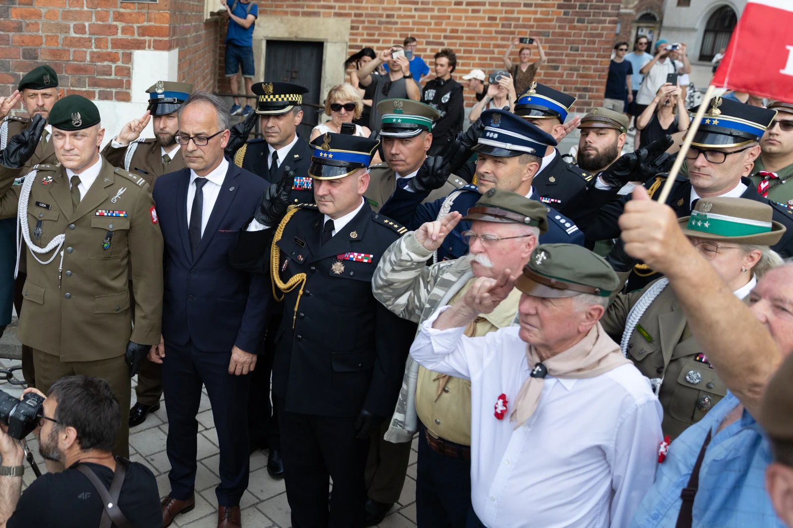 Grupa mężczyzn w mundurach i cywilnych strojach, salutujących podczas uroczystości. Autor: Bogusław Świerzowski