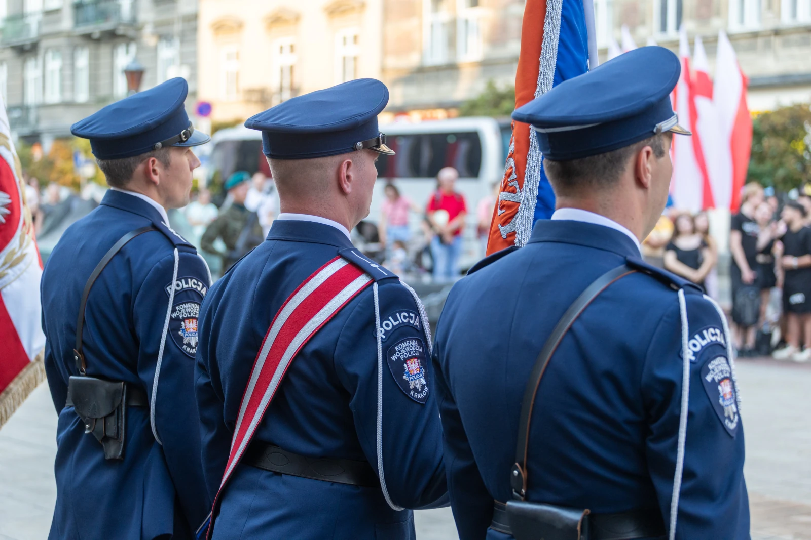 Trzech policjantów w mundurach, stojących z flagami na tle zgromadzenia ludzi. Autor: Bogusław Świerzowski