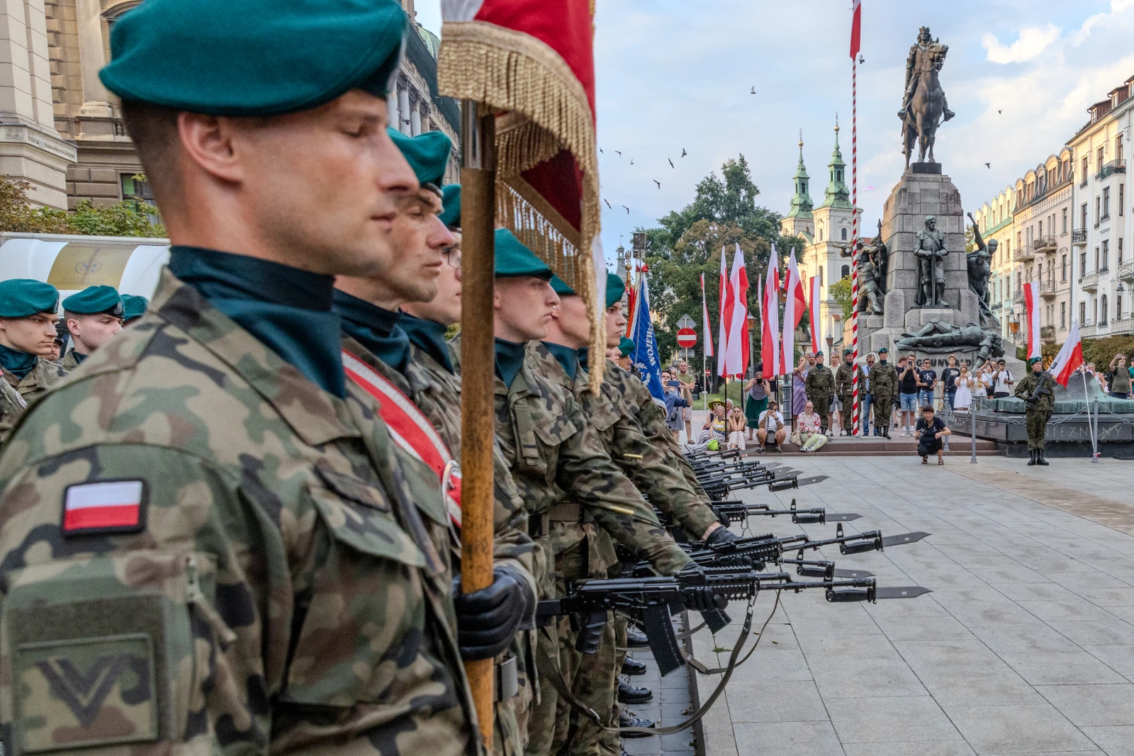 Żołnierze w mundurach wojskowych z bronią, stojący w szeregu podczas uroczystości z flagami. Autor: Bogusław Świerzowski