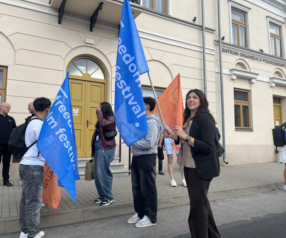 Grupa osób z niebieskimi flagami Freedom Film Festiwal przed budynkiem. O wydarzeniu przeczytasz na Eska Radom.
