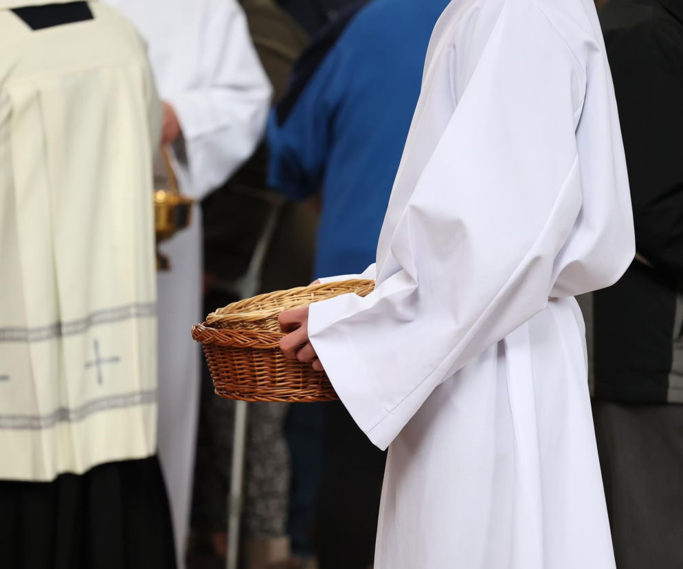 Ręce ministranta w białej albie trzymające wiklinowy koszyk na tace. O finansach kościoła przeczytasz na Eska Lublin.