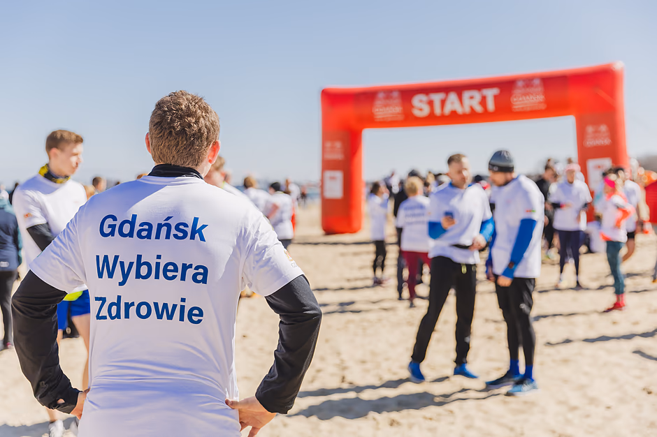 Gdańsk Biega i Wybiera Zdrowie - zbliżenie na mężczyznę w białej koszulce z napisem Gdańsk Wybiera Zdrowie