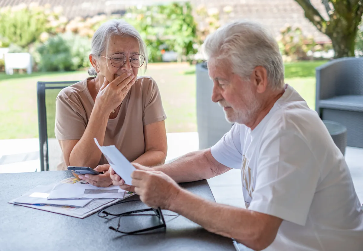 Seniorzy przynieśli listy, by otworzyć je przy stole. Mężczyzna czyta treść jednego z nich, kobieta jest wyraźnie przejęta. | Fot. Shutterstock.