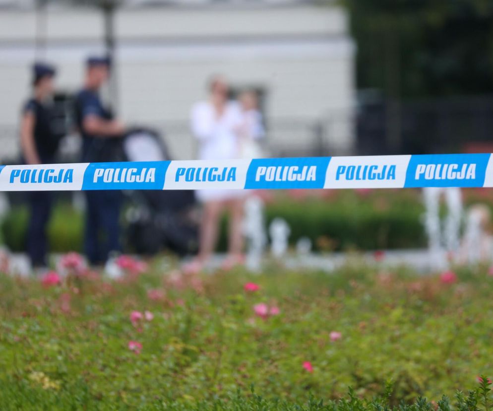 Biało-niebieska taśma policyjna na pierwszym planie. W tle niewyraźne sylwetki policjantów. Szczegóły na Eska Poznań.