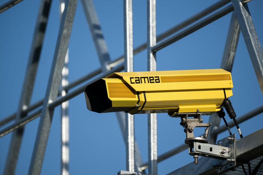 Kamera fotoradaru monitorująca koloru żółtego, zamontowana na metalowej konstrukcji, na tle nieba.
