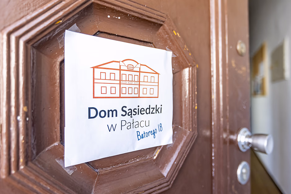 Dom Sąsiedzki w Pałacu - zbliżenie na tabliczkę wiszącą na drzwiach