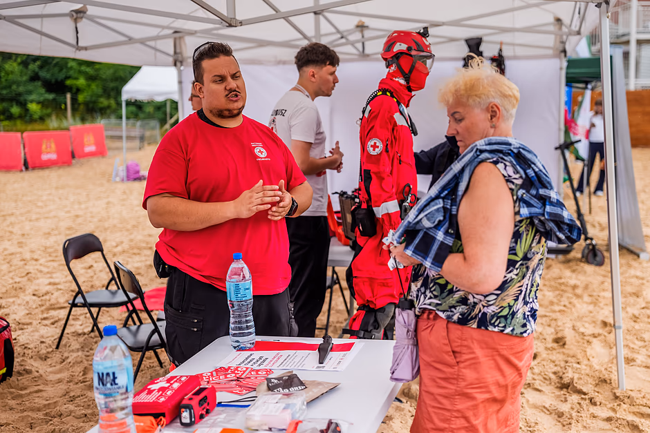 Dwie osoby rozmawiaja w czerwonym namiocie postawionym na plaży