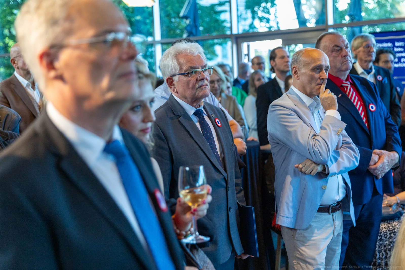 Grupa ludzi w eleganckich strojach, niektórzy trzymają kieliszki, w tle widoczne drzewa. Autor: Bogusław Świerzowski