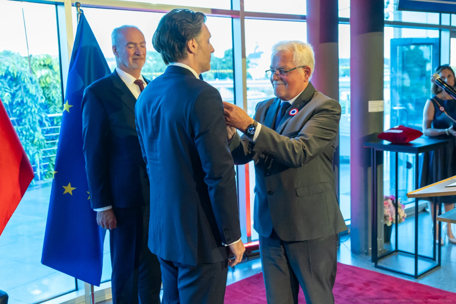Ceremonia wręczenia odznaczenia mężczyźnie w garniturze. W tle flagi i goście. Autor: Bogusław Świerzowski