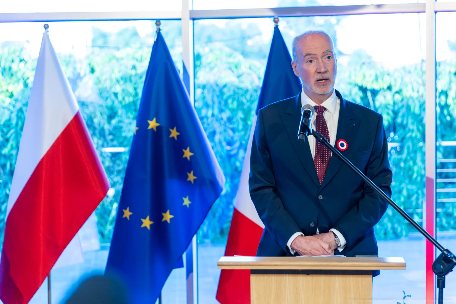 Mężczyzna przemawia przy mównicy, obok flagi Polski, Unii Europejskiej i Francji. Autor: Bogusław Świerzowski