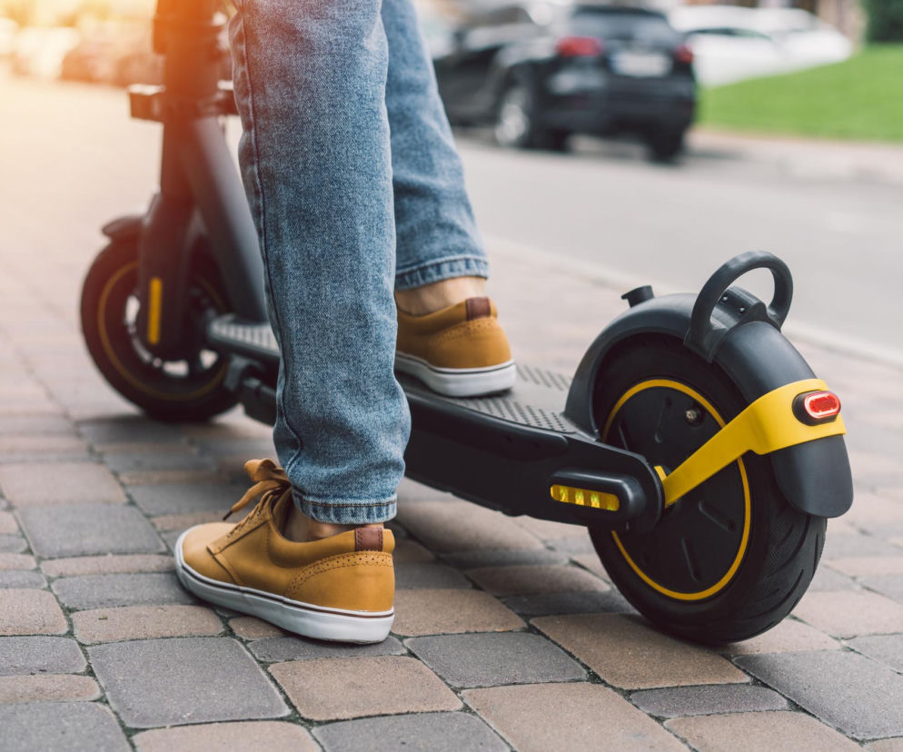 Nogi osoby w jeansach jadącej na hulajnodze elektrycznej po chodniku. O zatrzymaniu w Radomiu przeczytasz na Eska Radom.