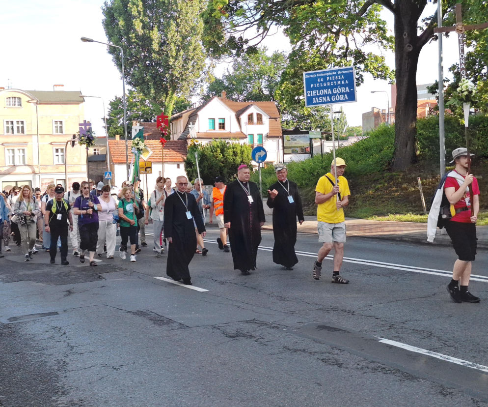 Bp Adrian Put i pielgrzymi idący ulicą z tablicą i krzyżami. O pielgrzymce na Jasną Górę przeczytasz na Radioplus.