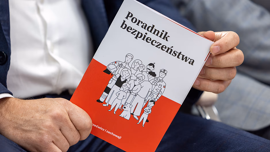 Dłonie mężczyzny trzymają książeczkę pt. Poradnik bezpieczeństwa .