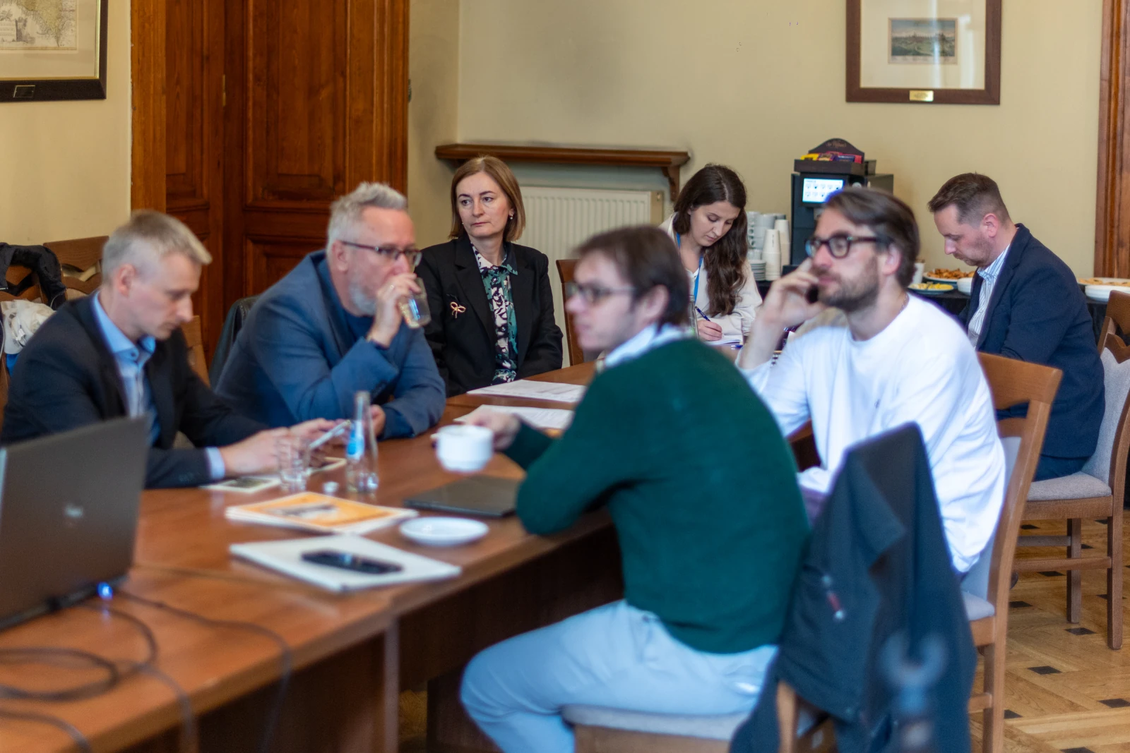 Grupa ludzi siedzących przy stole podczas spotkania, z laptopami i notatkami. Autor: Bogusław Świerzowski