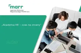 Trzech ludzi siedzi przy biurku w biurze, dyskutując i przeglądając dokumenty. Na stole są także laptop, telefon i kubek na kawę. Na zdjęciu widoczne jest logo MARR i napisy związane z "Akademią HR".