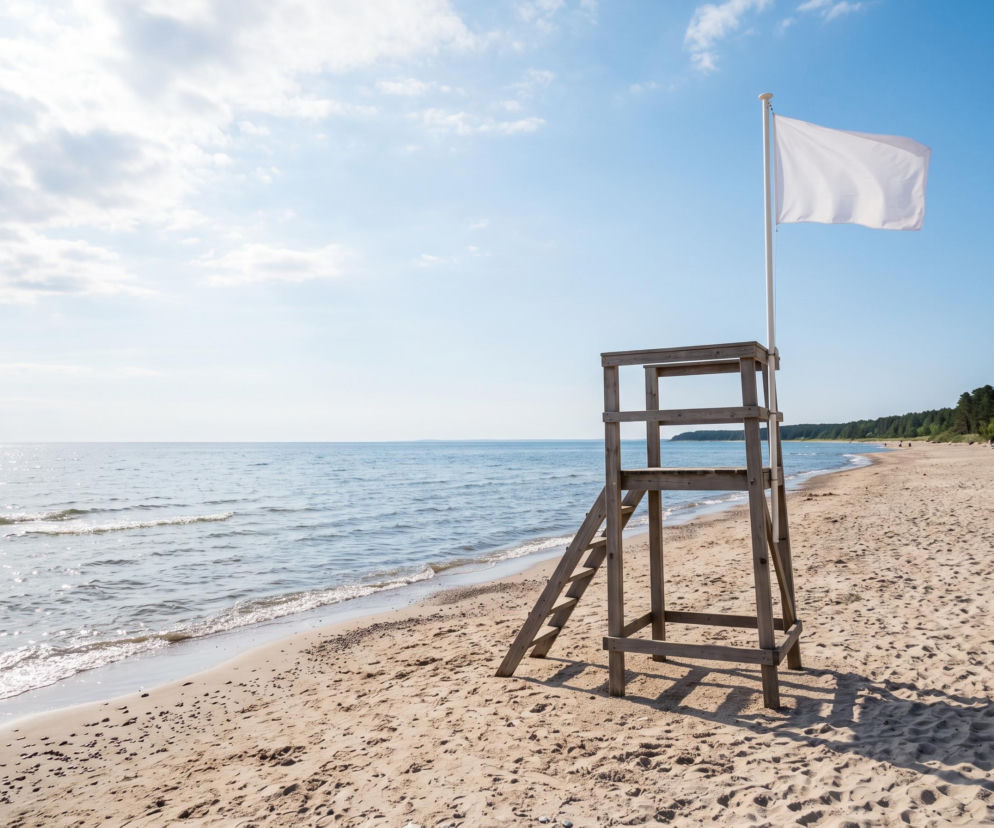 Biała flaga na wieży ratowniczej przy pustej plaży w Chłopach. O warunkach nad morzem przeczytasz na SE Szczecin.