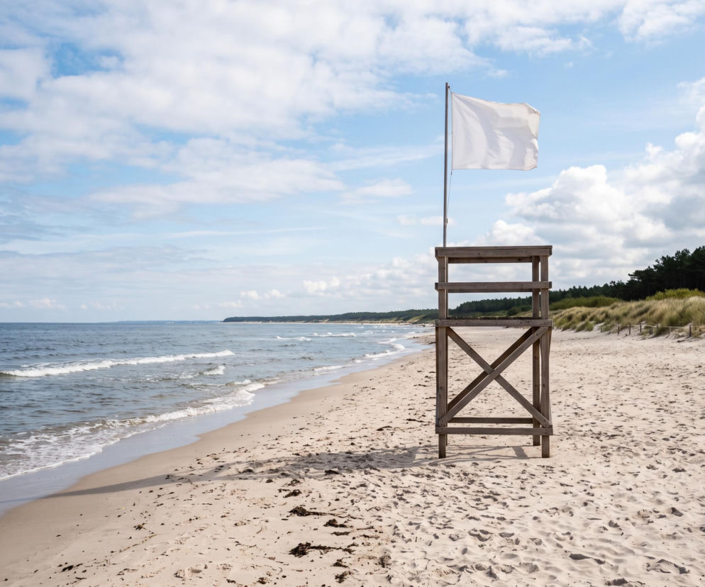Drewniana wieża ratownicza z białą flagą na pustej plaży w Dąbkach. O bezpieczeństwie nad morzem przeczytasz na SE Szczecin.