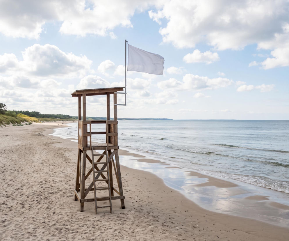 Drewniana wieża ratownicza z białą flagą na pustej plaży w Darłowie. O warunkach nad morzem przeczytasz na SE Szczecin.
