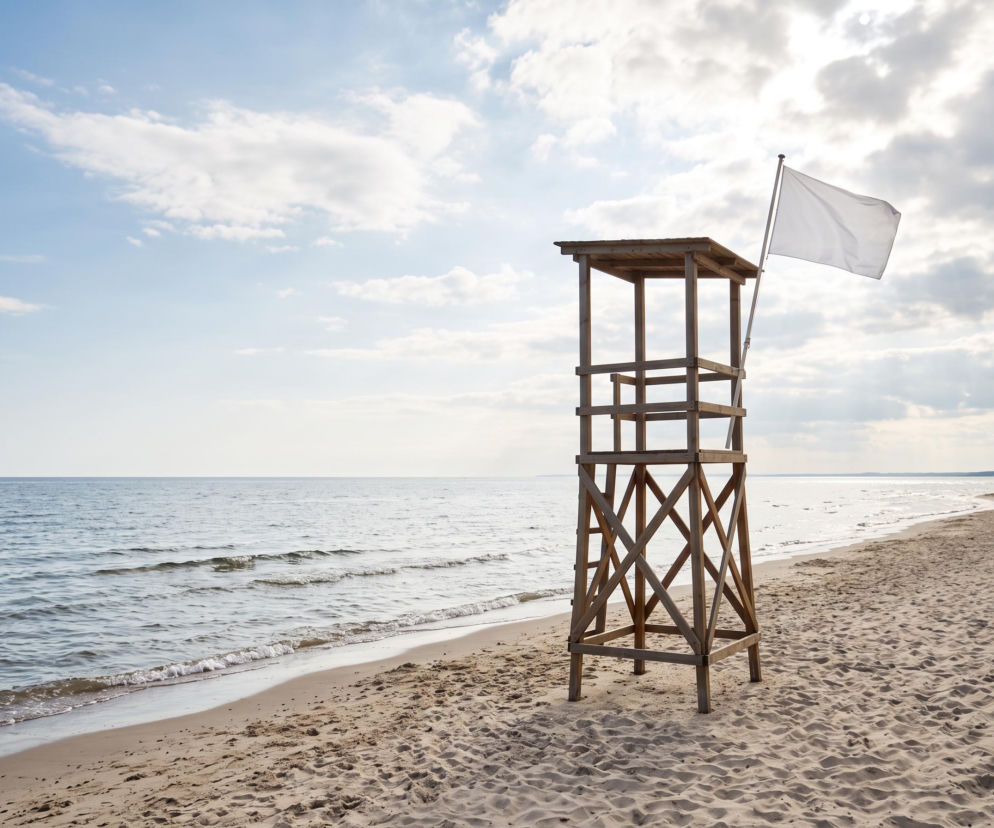 Drewniana wieża ratownicza z białą flagą na pustej plaży w Darłowie. O pogodzie nad morzem przeczytasz na SE Szczecin.