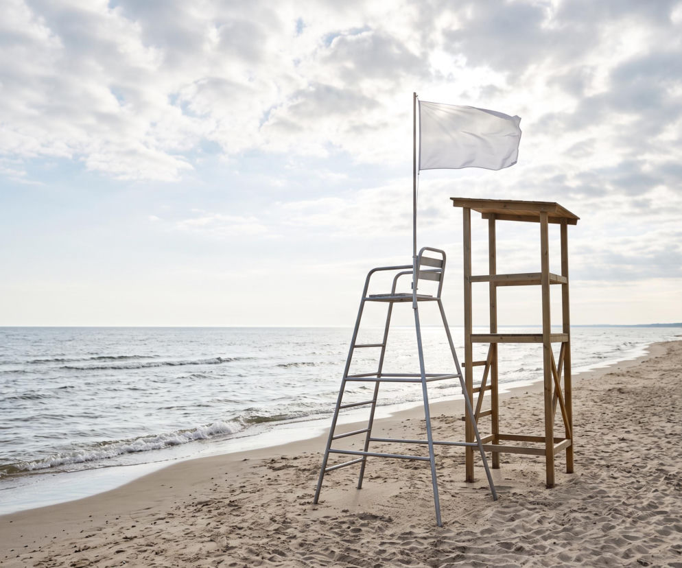 Biała flaga na wieży ratowniczej na pustej plaży w Dźwirzynie. O braku sinic i pogodzie przeczytasz na SE Szczecin.