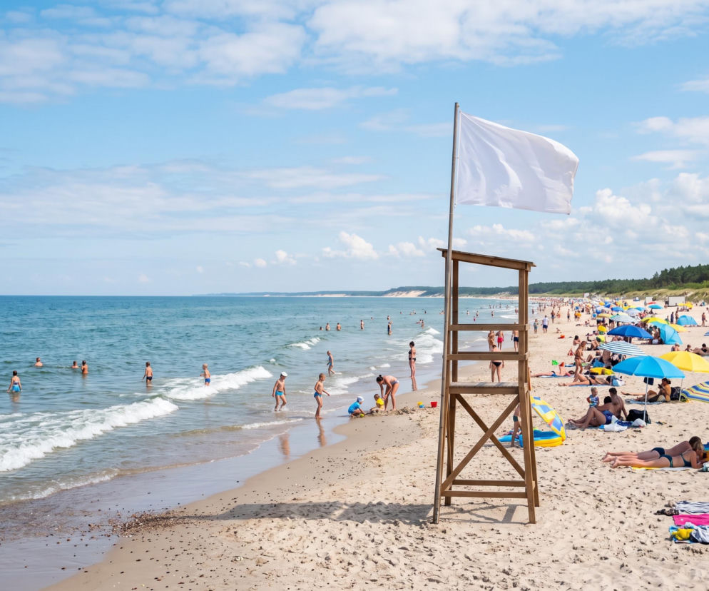 Biała flaga na wieży ratowniczej nad pełną ludzi plażą w Dźwirzynie. O braku sinic przeczytasz na SE Szczecin.
