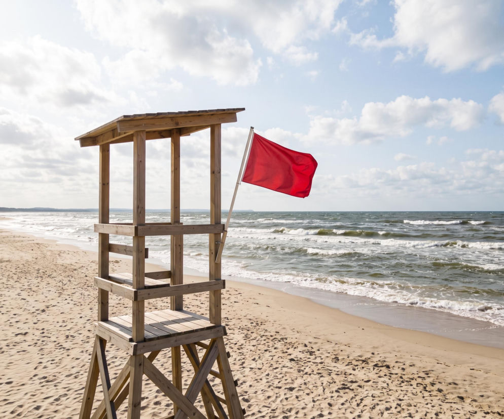 Drewniana wieża ratownicza na plaży z czerwoną flagą oznaczającą zakaz kąpieli. O plażach w Gdańsku czytaj w Eska Trójmiasto.