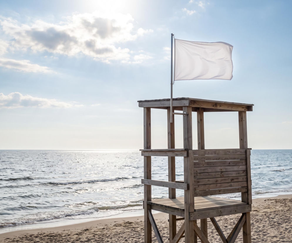 Drewniana wieża ratownicza z białą flagą na pustej plaży w Gdyni. O bezpiecznej kąpieli przeczytasz na Eska Trójmiasto.