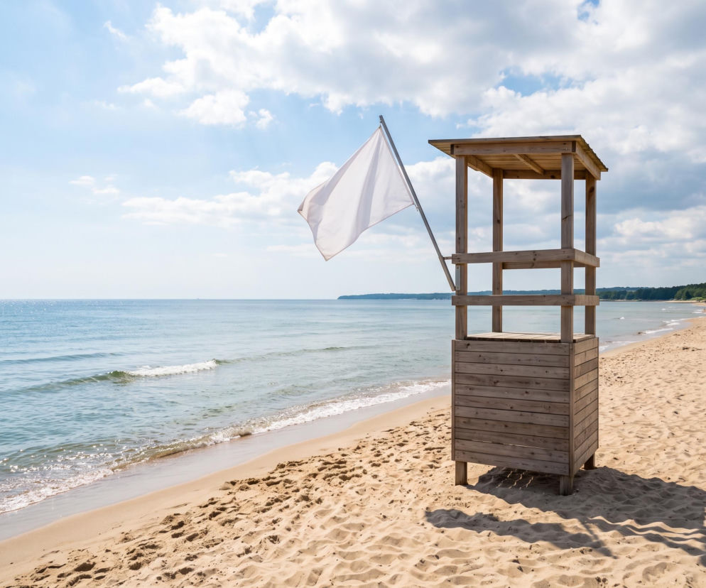 Drewniana wieża ratownicza z białą flagą na pustej plaży w Gdyni. O czystej wodzie przeczytasz na Eska Trójmiasto.