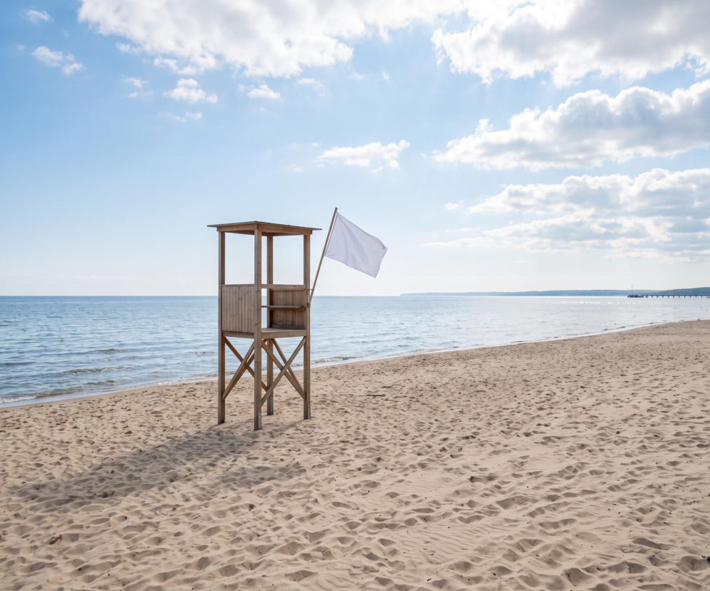 Drewniana wieża ratownicza z białą flagą na pustej plaży w Gdyni. O czystości wody przeczytasz na Eska Trójmiasto.