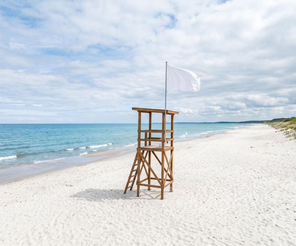 Biała flaga na wieży ratowniczej na pustej, piaszczystej plaży. O pogodzie i kąpieliskach przeczytasz na Eska Trójmiasto.
