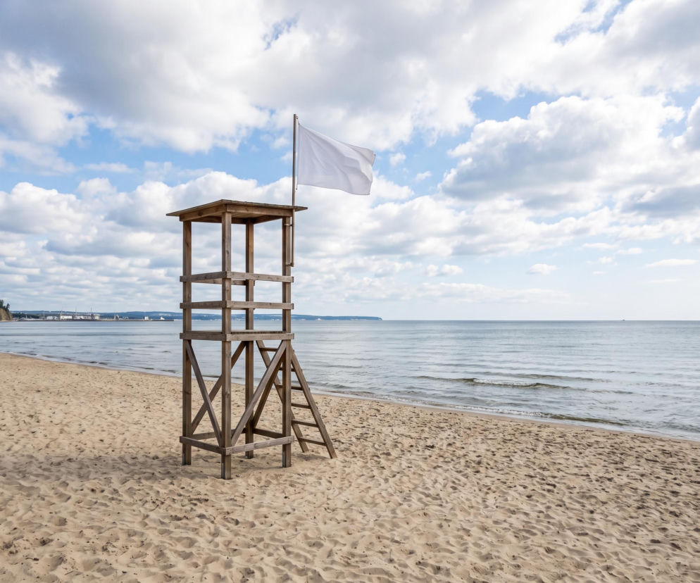 Drewniana wieża ratownicza z białą flagą na pustej plaży w Gdyni. O czystej wodzie przeczytasz na Eska Trójmiasto.