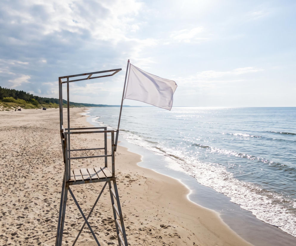 Biała flaga na wieży ratowniczej przy pustej plaży w Grzybowie. O warunkach nad morzem przeczytasz na SE Szczecin.