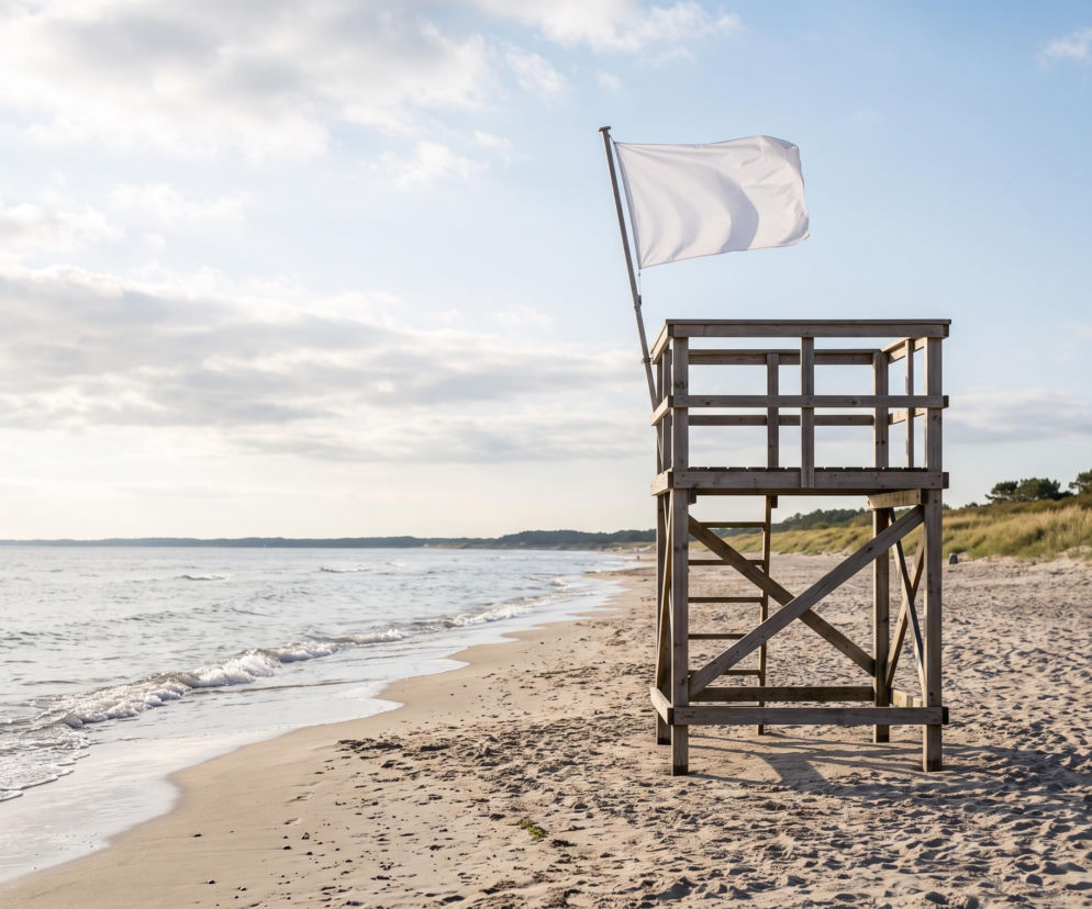 Drewniana wieża ratownicza z białą flagą na pustej plaży. O bezpieczeństwie w Krynicy Morskiej przeczytasz na Eska Trójmiasto.