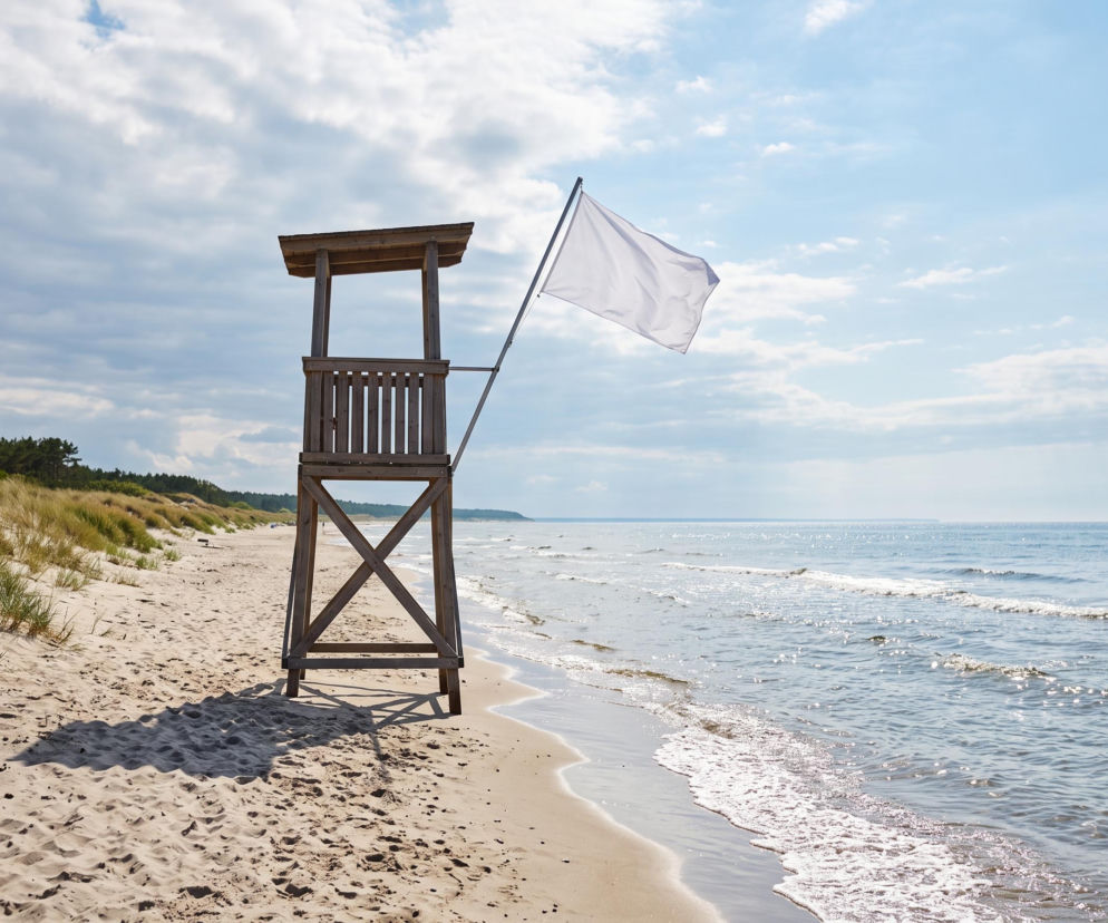 Drewniana wieża ratownicza z białą flagą na plaży w Łazach. O warunkach nad wodą przeczytasz na SE Szczecin.
