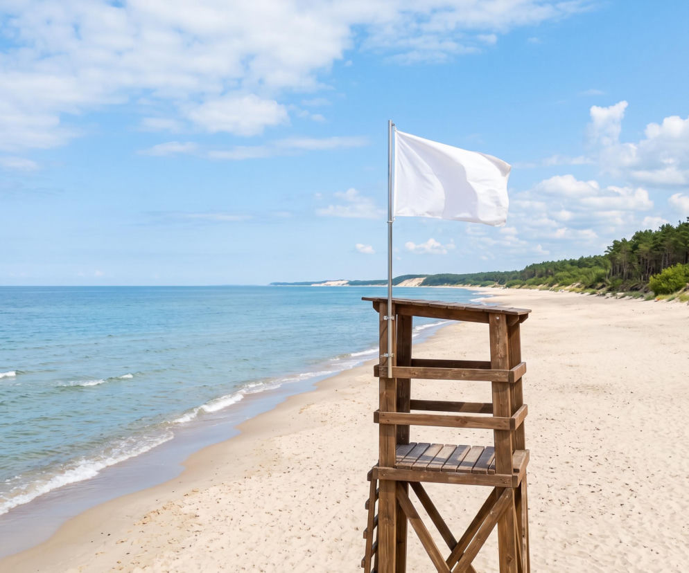 Biała flaga na wieży ratowniczej przy pustej plaży w Łazach. O warunkach nad morzem przeczytasz na SE Szczecin.