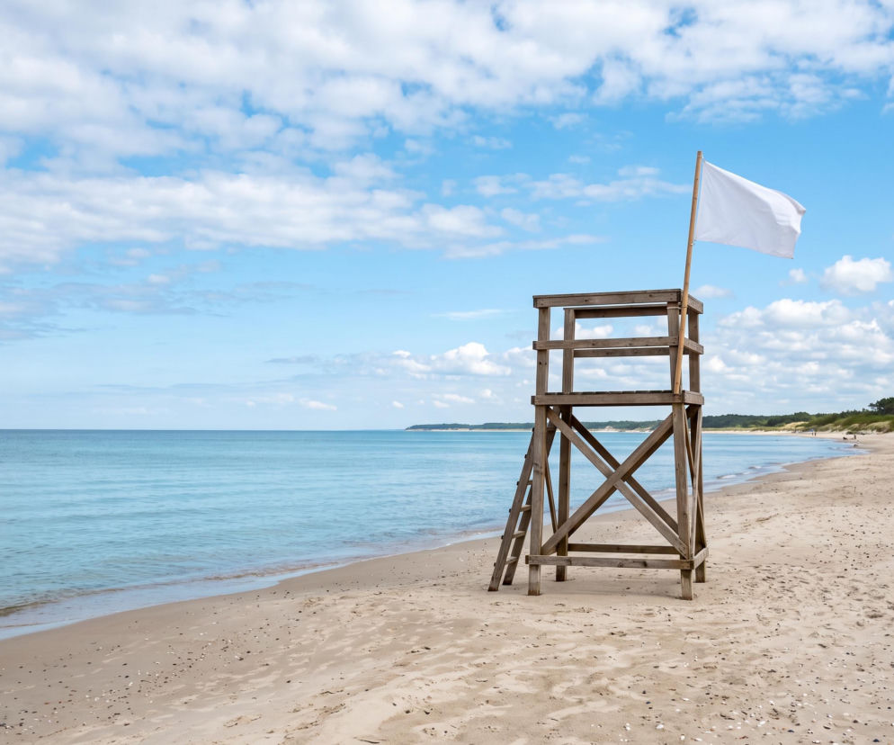 Drewniana wieża ratownicza z białą flagą na pustej plaży w Łazach. O warunkach kąpieli przeczytasz na SE Szczecin.