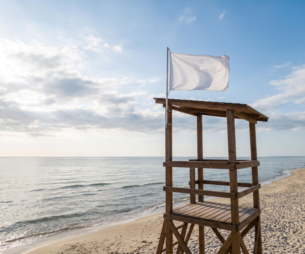 Biała flaga na drewnianej wieży ratowniczej na pustej plaży w Łebie. O warunkach kąpieli przeczytasz na Eska Trójmiasto.