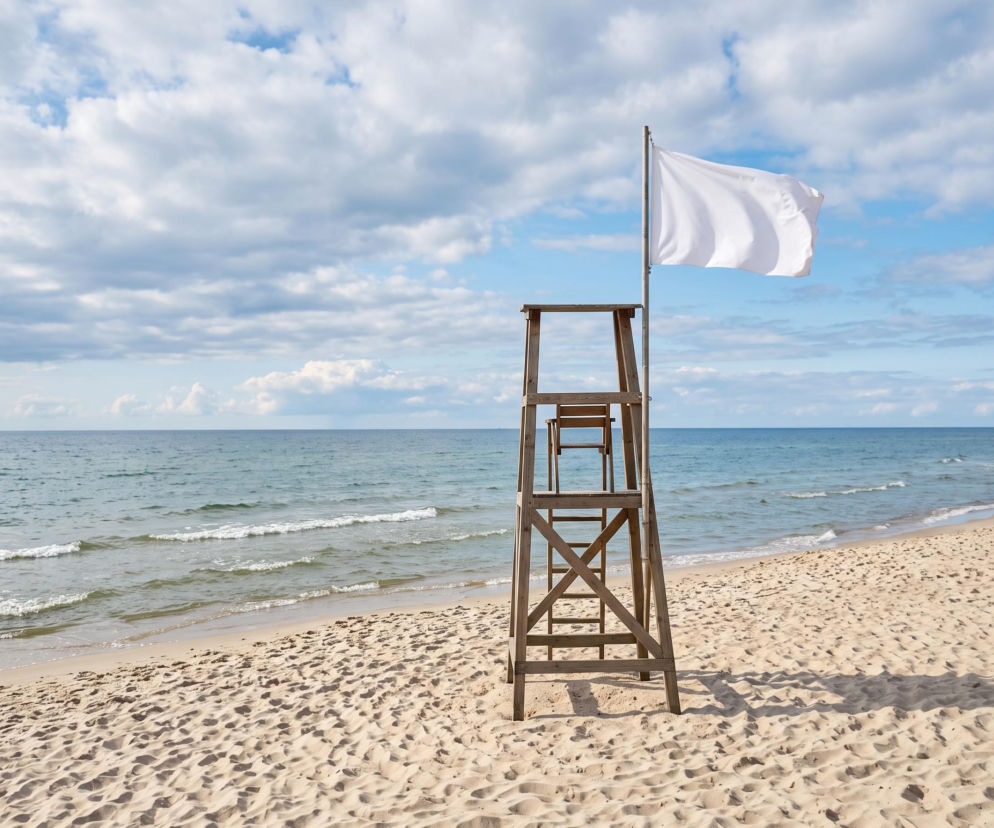 Biała flaga na wieży ratowniczej przy pustej plaży w Łebie. O warunkach nad morzem przeczytasz na Eska Trójmiasto.
