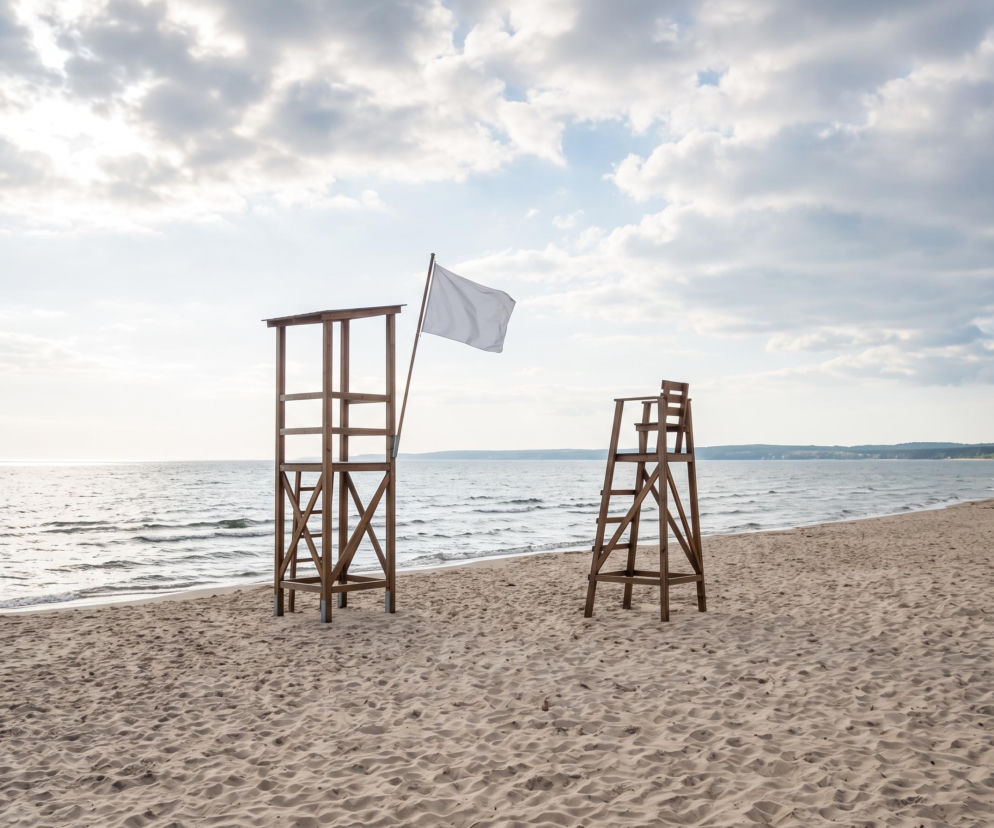 Pusta piaszczysta plaża w Mechelinkach z wieżą ratowniczą i białą flagą. O czystości wody czytaj w Eska Trójmiasto.
