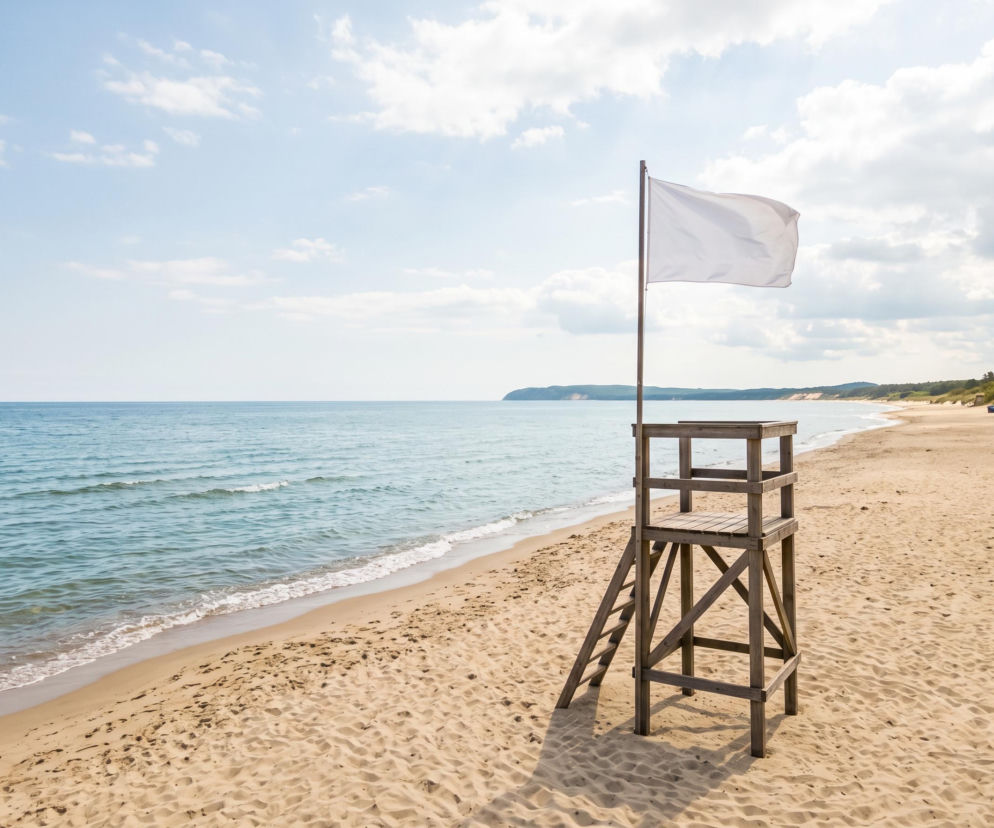 Wieża ratownicza z białą flagą na pustej piaszczystej plaży. O pogodzie w Mechelinkach przeczytasz na Eska Trójmiasto.