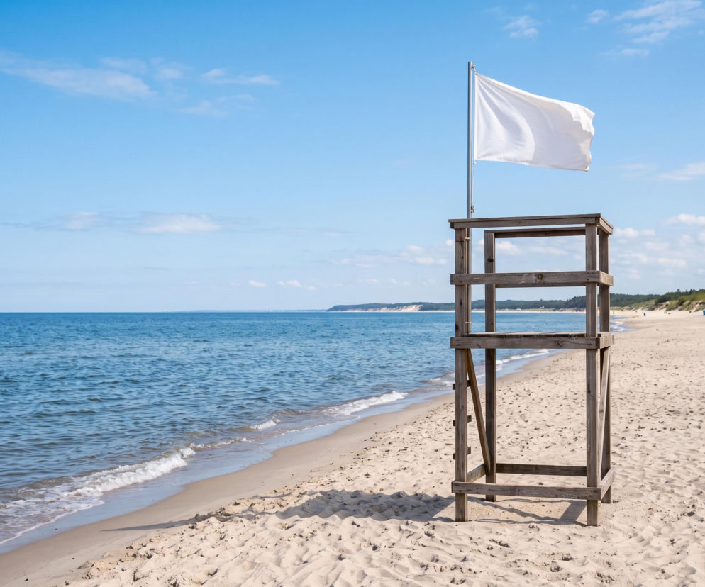 Drewniana wieża ratownicza z białą flagą na pustej plaży w Międzyzdrojach. O bezpieczeństwie kąpieli czytaj w SE Szczecin.