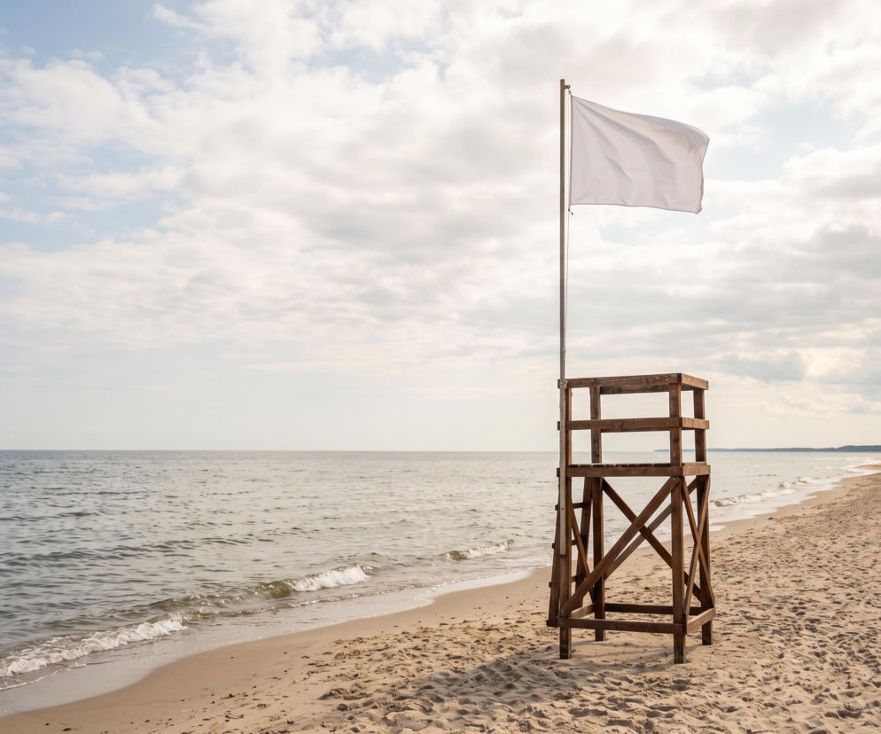 Drewniana wieżyczka ratownicza z białą flagą na pustej plaży w Mielnie. O otwartych kąpieliskach dowiesz się z SE Szczecin.