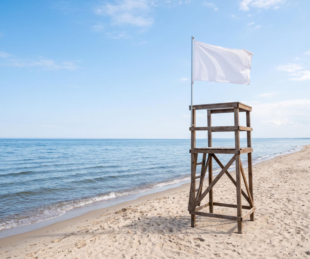 Drewniana wieża ratownika z białą flagą na pustej plaży. O bezpiecznej kąpieli w Rewie przeczytasz na Eska Trójmiasto.