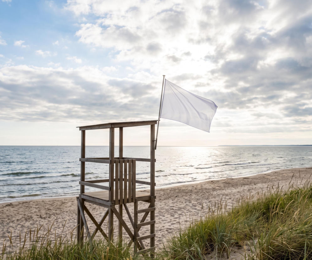 Drewniana wieża ratownika z białą flagą na pustej plaży. O bezpieczeństwie kąpieli w Rewie przeczytasz na Eska Trójmiasto.