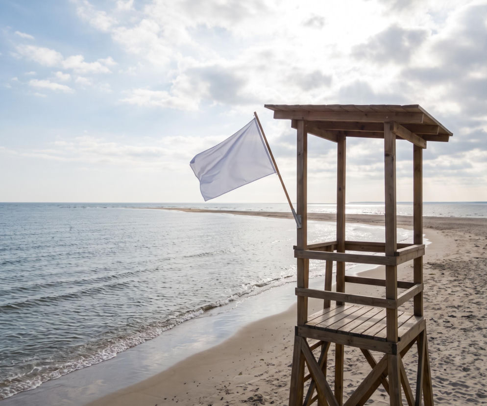 Drewniana wieża ratownicza na plaży w Rewie z białą flagą. O bezpieczeństwie nad wodą przeczytasz na Eska Trójmiasto.