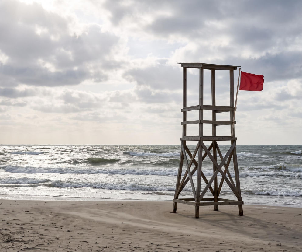 Wieża ratownicza z czerwoną flagą na plaży w Rewie przy wzburzonym morzu. O zakazie kąpieli informuje Eska Trójmiasto.