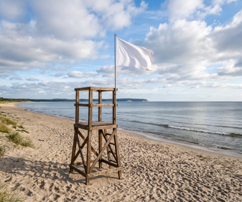 Drewniana wieża ratownicza z białą flagą na pustej plaży w Rewie. O czystej wodzie bez sinic przeczytasz na Eska Trójmiasto.