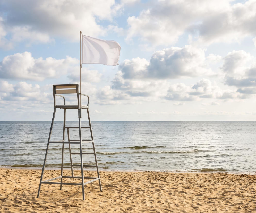 Wieża ratownicza z białą flagą na piaszczystej plaży nad morzem. O warunkach w Rewie przeczytasz na Eska Trójmiasto.