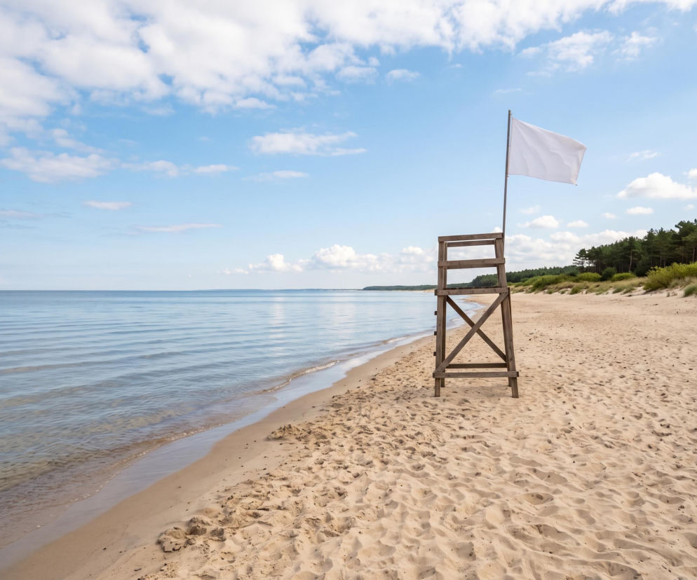 Pusta piaszczysta plaża w Rowach z białą flagą na wieży ratowniczej. O warunkach kąpieli przeczytasz na Eska Trójmiasto.